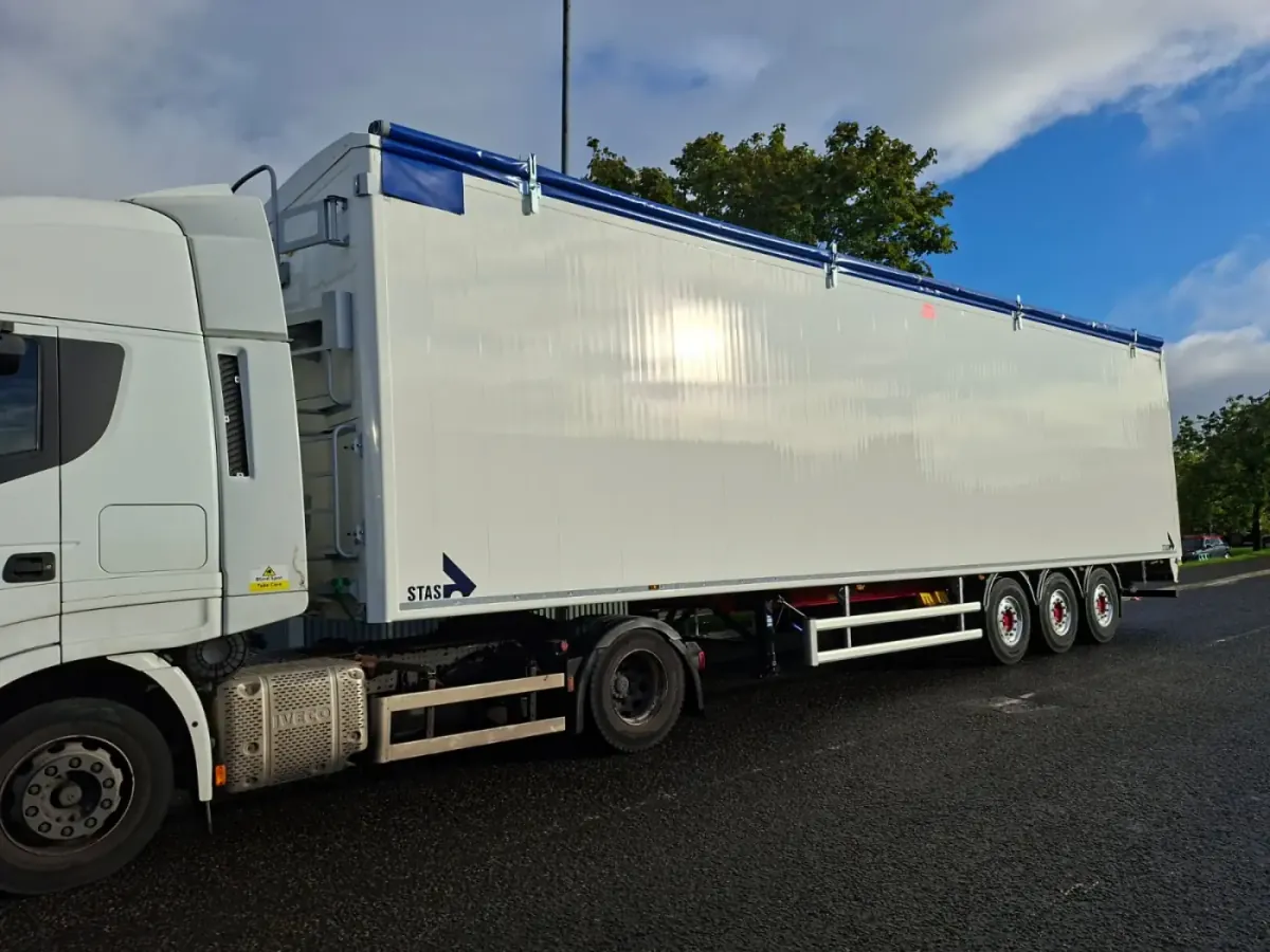 White tractor unit coupled to a sheeted bulk trailer under a bright blue sky